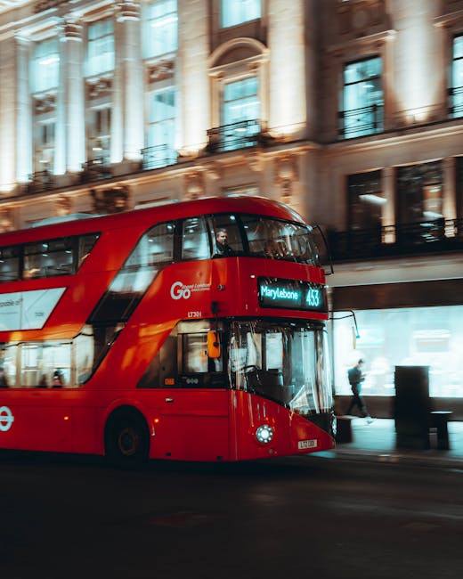 A red double-decker London bus, part of the Go service, is pictured driving along a city street outside a historic building with ornate architectural details and large windows. The bus displays a digital route sign indicating it is heading to Marylebone. The scene is illuminated by ambient street lighting, reflecting the urban environment during dusk or evening. Behind the bus, pedestrians are visible walking on the sidewalk, some passing near the entrance of the building. The image captures a moment of home relocation or moving logistics context, subtly highlighting transportation aspects related to furniture transport and moving services provided by Man with Van Marylebone, with the focus on the busy city backdrop as part of the visual narrative.