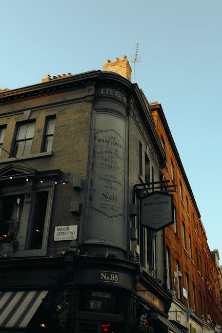 Photograph of a historic building at the corner of a street in Marylebone during daylight, featuring a rounded facade with signage for The Marylebone and No. 98. The building's exterior is painted in 